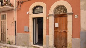 Un edificio con una porta in legno, una finestra con inferriata metallica e una targa con il numero.