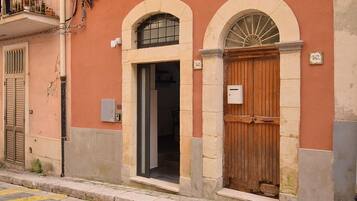 Un edificio con una porta in legno, una finestra con inferriata metallica e una targa con il numero.