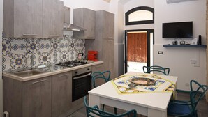 Una cucina con piano cottura a gas, lavello e pensili, un tavolo da pranzo con sedie e una TV a parete.