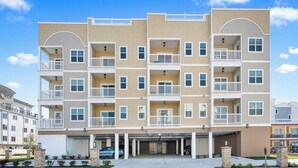 A multi-story residential building with balconies, a covered parking area, and a clear sky. - Residence 103N at The Sandcastle Condominiums (Wildwood Crest)