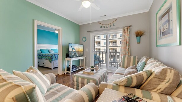 A living room with striped sofas, a TV, a desk, and a balcony with a view. - Residence 103N at The Sandcastle Condominiums (Wildwood Crest)