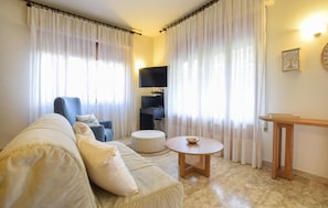 A living room with a sofa, a round table, a chair, and a television.