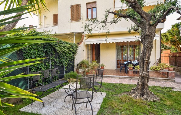 A courtyard with a table and chairs, a tree, and a building with a balcony.