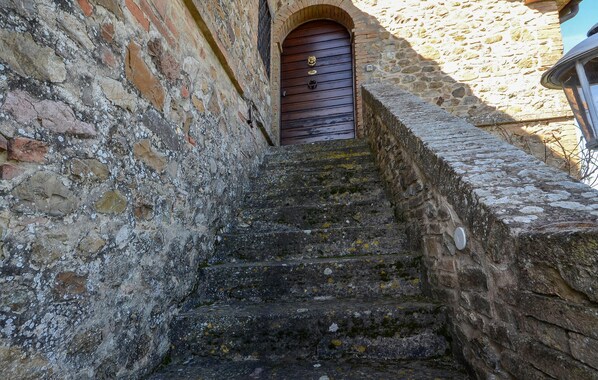 Una escalera de piedra conduce a una puerta de madera con un llamador de latón, enmarcada por paredes de piedra antiguas.