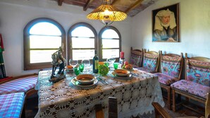 A dining area with a table set for two, featuring a lace tablecloth, wooden chairs, and a hanging light fixture. - La Duchessa Tenuta Donna Olga (Porrona)
