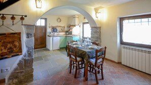 A dining area with a table set for four, a kitchen in the background, stone arches, and a window with a view. - Lovely home in Casidore with WiFi (Casidore)