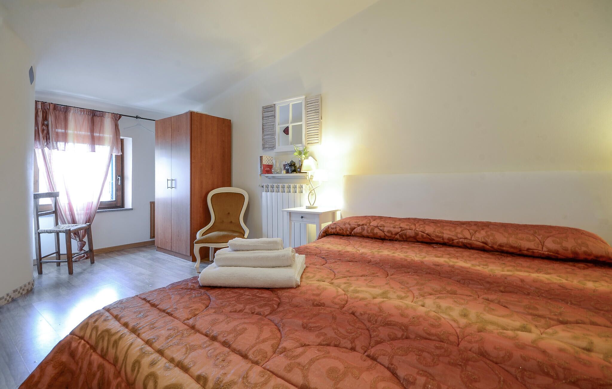Habitació d'hotel amb un llit, una cadira, un escriptori i una finestra amb cortines.