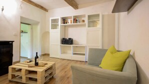Un salon avec un canapé gris, une table basse en bois sur laquelle se trouve une bouteille de vin, une étagère blanche et un haut-parleur noir.