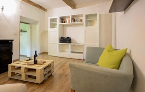 A living room with a grey sofa, a wooden coffee table with wine, a white shelving unit, and a black speaker.