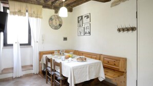 Un coin repas avec un banc en bois, une table recouverte d’une nappe blanche et une horloge murale.
