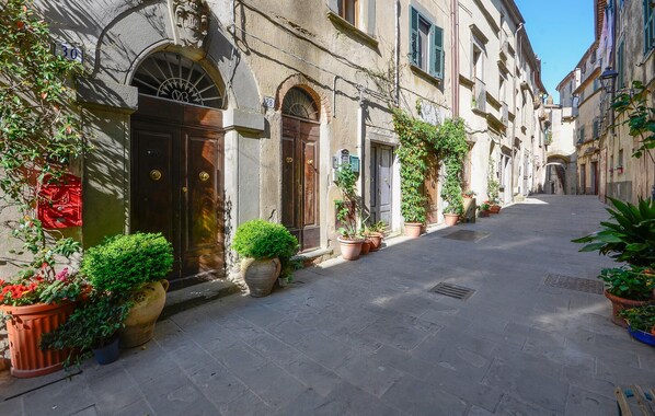 A narrow street lined with historic buildings, potted plants, and a clear sky.