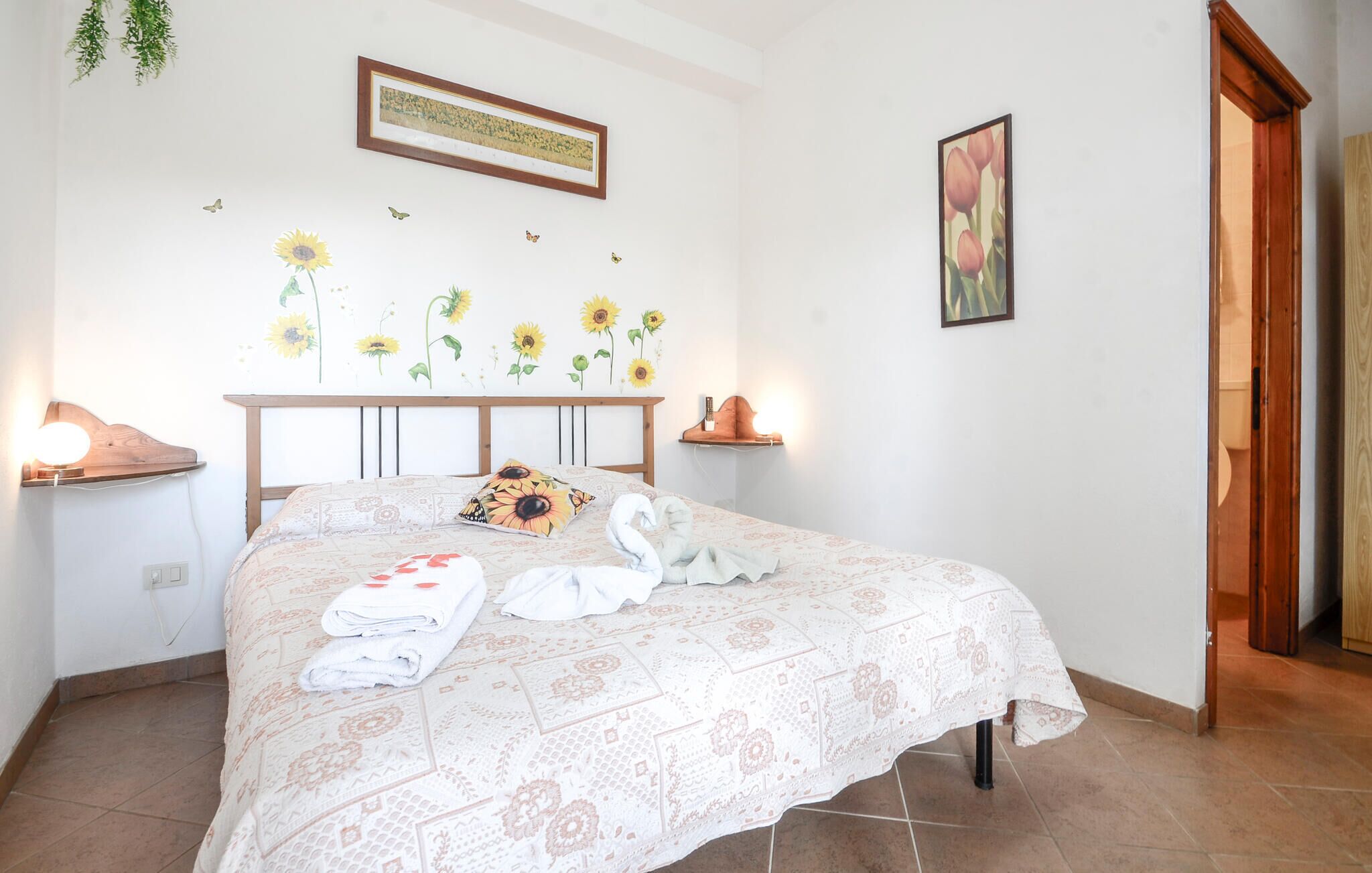 Una cama bien hecha con una colcha estampada, un cuadro colgado en la pared y una decoración de girasoles.