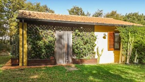 Une maison de plain-pied avec un toit en tuiles, une porte surmontée d’un portail en métal et une petite fenêtre avec des volets.
