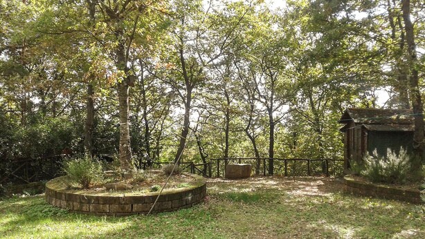 Une zone boisée comprenant une structure en pierre, une clôture en métal et un élément circulaire en pierre.