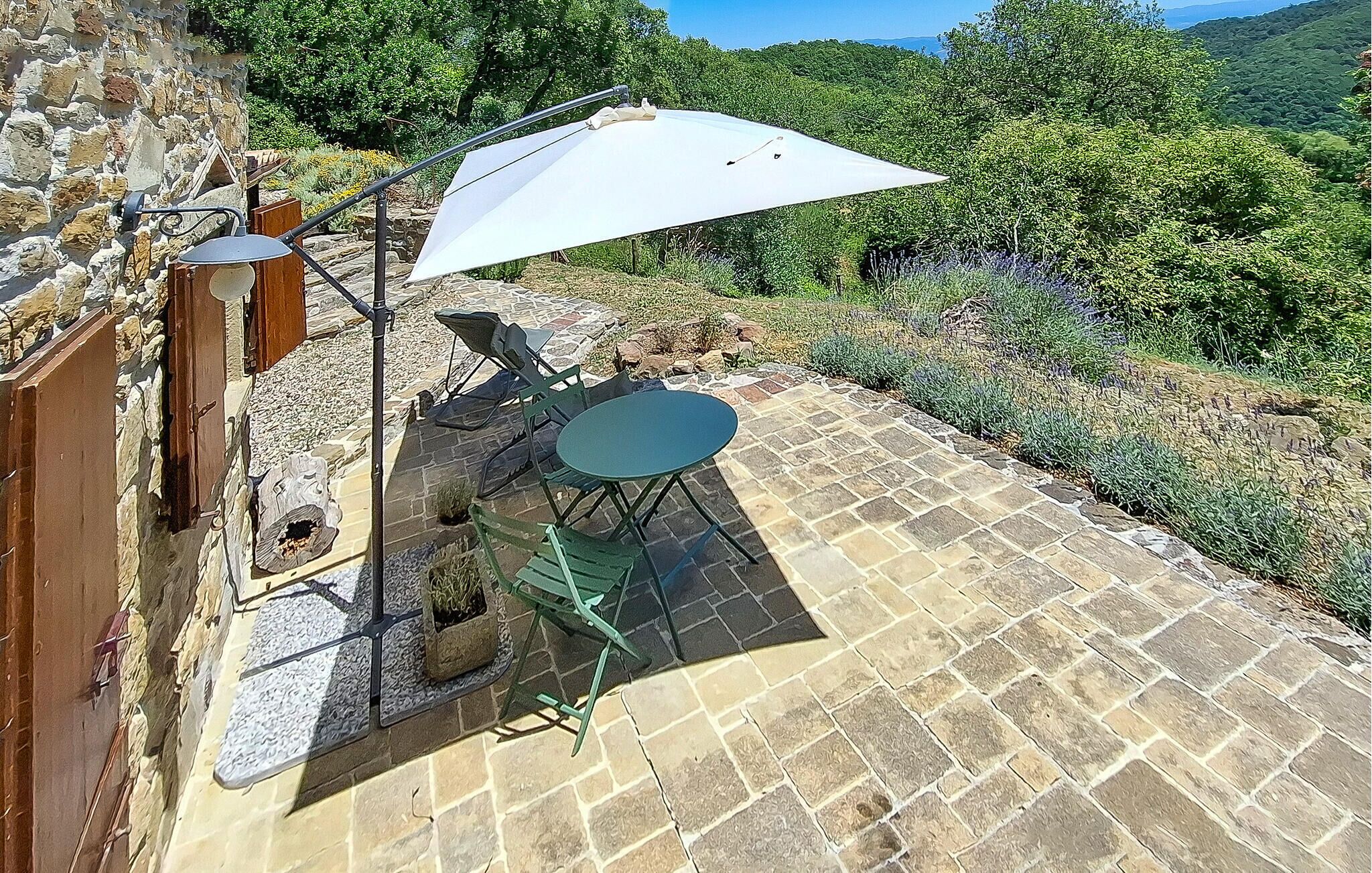 A stone patio with a table and chairs, a white umbrella, and a stone wall.
