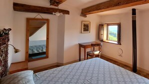 Une chambre à coucher avec un lit, un plafond en bois, une fenêtre donnant sur un beau paysage, un bureau et une chaise.