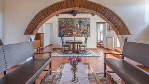Un coin repas agrémenté d’une arche en briques, d’une table avec des chaises, d’un grand tableau au mur et d’un vase de fleurs posé sur la table.