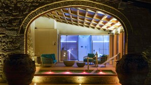 Uma entrada em arco com parede de pedra, piscina com um elemento aquático e área de estar com cadeiras e mesa.