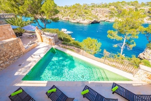 A pool with a view of the sea, outdoor seating, and a stone wall.