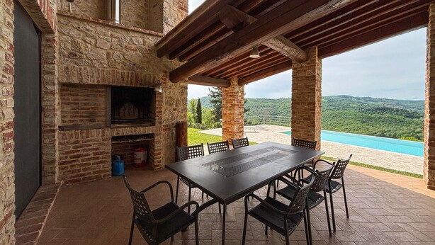 Edifici de pedra amb una llar de foc de rajola, una taula amb cadires i vista a una piscina blava i turons verds.