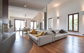 A spacious living area with a large sectional sofa, a dining table, and a kitchen area with a stone wall. - Nice home in San Venanzo (San Venanzo)