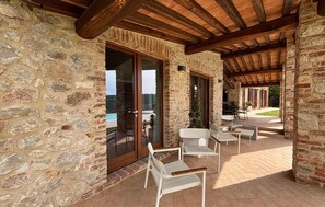 A stone building with a wooden ceiling, a glass door, and outdoor seating. - Nice home in San Venanzo (San Venanzo)