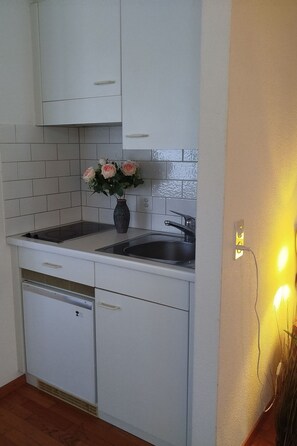 Eine kompakte Küche mit weißen Schränken, einer eingebauten Spüle und einem kleinen Kühlschrank.
