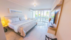 Ein modernes Schlafzimmer mit Bett, Fernseher, Sofa und einem Balkon mit Gartenmöbeln.