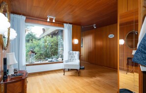 Ein Zimmer mit Holzwänden, einem großen Fenster mit Vorhängen, einem weißen Sessel und einem Holzboden.