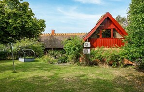 Ein rotes Haus mit Strohdach, umgeben von Grünpflanzen und einem Garten.