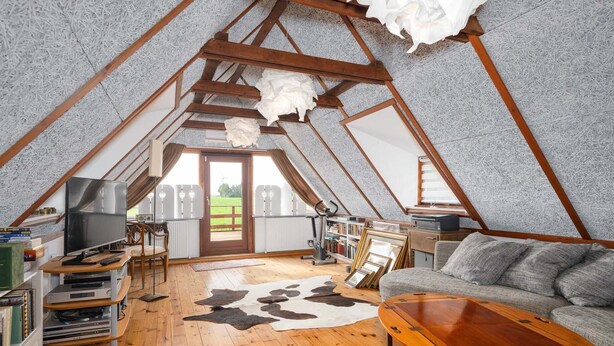 Um quarto de sótão aconchegante com teto inclinado, vigas de madeira, uma televisão, um sofá, uma mesa de centro e um tapete de couro bovino.