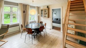 En matplats med ett runt bord, stolar, en hängande lampa, ett skåp med glasdörrar och en trappa.
