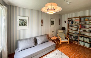 A cozy living room with a grey sofa, striped wallpaper, a bookshelf, and a hanging light fixture.