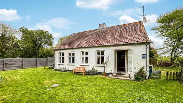 Ett tvåvåningshus med ett tak täckt av takpannor, en ytterdörr och en liten veranda med en bänk.