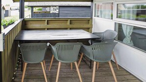 A wooden deck with a table and four chairs, a window, and a view of the street.