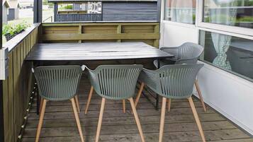 Une terrasse en bois avec une table et quatre chaises, une fenêtre et une vue sur la rue.