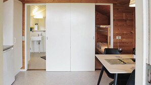 A room with a bed, a table with chairs, a white wardrobe, and a small kitchenette.