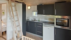 Une cuisine de taille réduite, avec des meubles de couleur sombre, un four encastré et une échelle appuyée contre le mur.