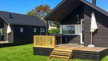 Une cabane moderne dotée d’une terrasse, d’un petit espace salon extérieur et d’une fenêtre bien visible.