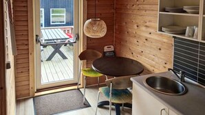 A compact kitchen with a dining area, a hanging light fixture, and a view of the deck.