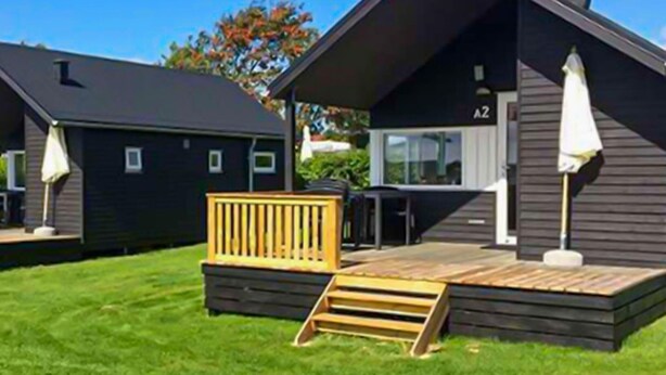 Una cabaña moderna con un balcón, un pequeño espacio de estar exterior y un ventanal visible.