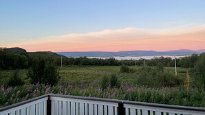 Vista panorámica desde un balcón con un campo de flores moradas, una masa de agua distante y montañas al fondo.