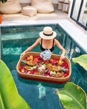 Eine Person im Pool hält einen schwimmenden Korb mit Essen und Blumen.