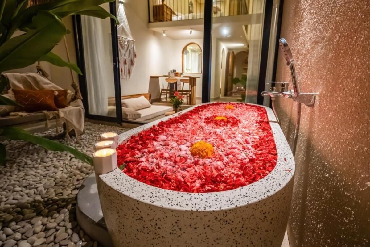 Wellnessbereich mit Whirlpool, umgeben von Rosenblättern, eine Sitzecke mit Sofa und Sesseln sowie ein Blick ins Innere.