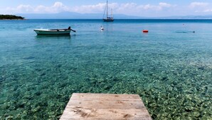 A wooden dock extending into clear, shallow water with a boat and a sailboat anchored in the distance. - Apartment Mladen - 1 by Interhome (Krk/Njivice)