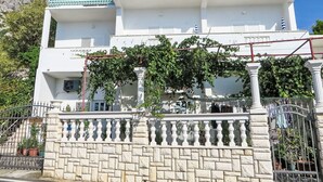 A multi-story building with a white facade, green-tiled balconies, and a stone wall with a wrought iron gate. - Gemütliche Ferienwohnung in Strandnähe by Interhome (Drašnice)