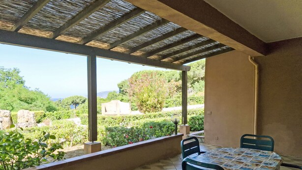 A covered patio with a table and chairs, overlooking a garden and distant landscape. - Wohnung mit Wasserblick by Interhome (Capoliveri)