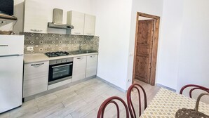 A compact kitchen with a gas stove, oven, and white cabinetry. A dining area with a patterned table and chairs is visible. - Wohnung mit Wasserblick by Interhome (Capoliveri)