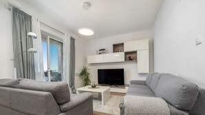 Una sala de estar moderna con sofás grises, un televisor de pantalla plana y una mesa de centro blanca.