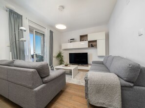 Ein modernes Wohnzimmer mit grauen Sofas, einem Flachbildfernseher und einem weißen Couchtisch.